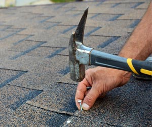 Worker Installing Roof Shingles With Hammer
